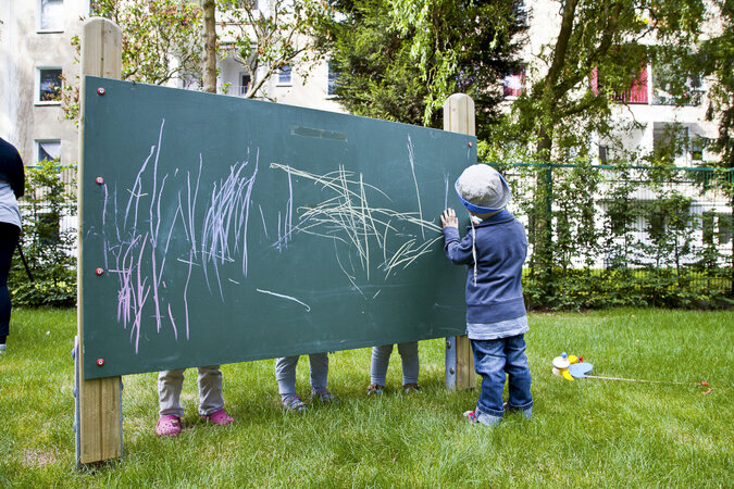 Kindergartenkind bemalt große Tafel auf einer Grünfläche. 