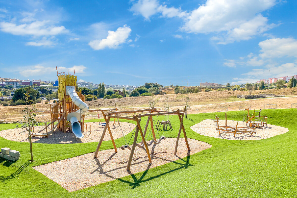 Öffentliche Spielanlagen – eibe Spielanlage auf einer gepflegten Grünfläche vor einer städtischen Kulisse. 
