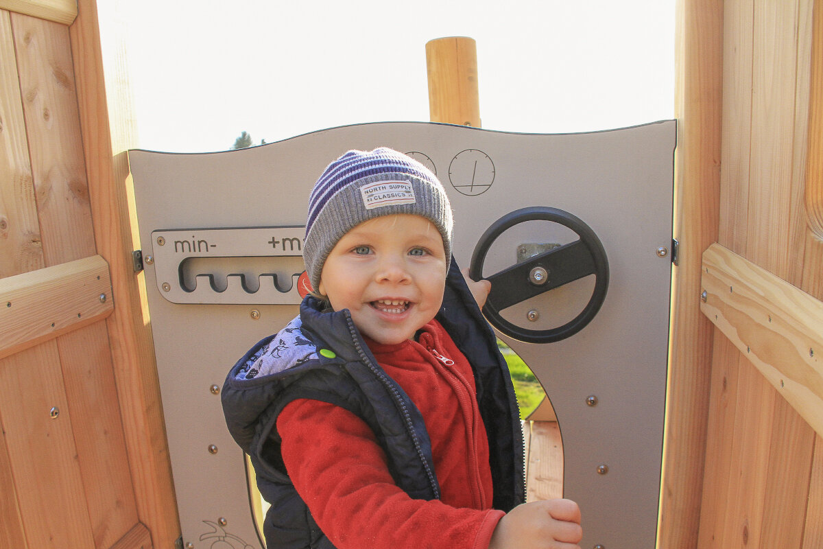 Kindergarten-Spielgeräte von eibe – Kindergartenkind lacht auf Spielturm in die Kamera.
